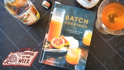 Batch Cocktails cookbook on a table with two liquor bottles and a cocktail.