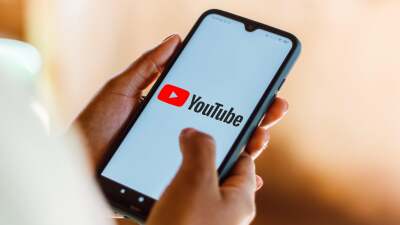 Person holding phone with YouTube logo on it.