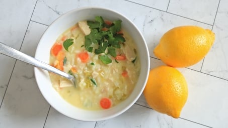 A bowl of avgolemono soup next to two lemons.