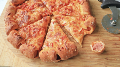 A hot dog-stuffed crust pizza on a cutting board.
